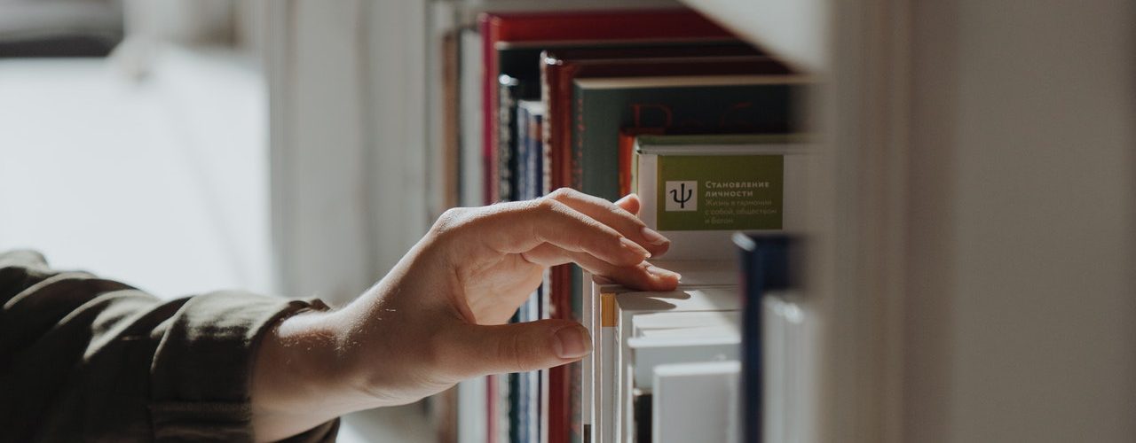 Person picking a book from a book shelf