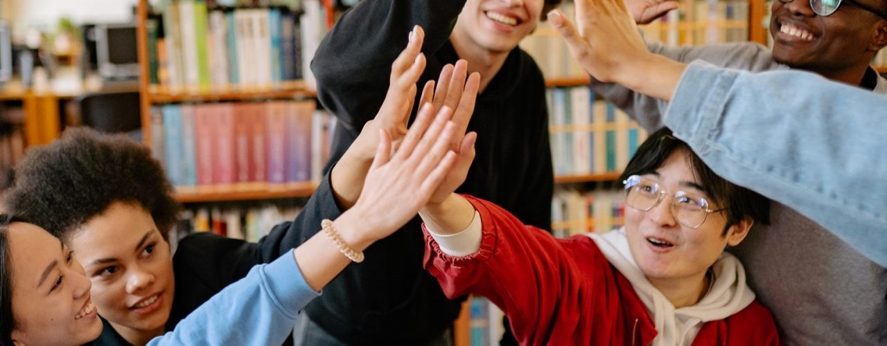 Group of diverse people sitting down high fiving in an office